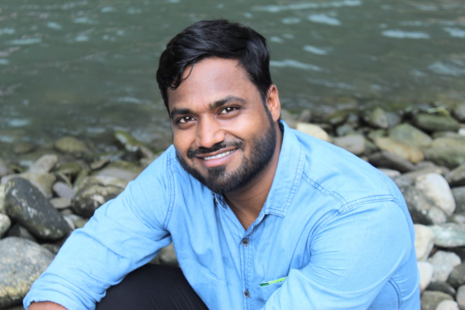 Sourabh Chanchal smiling, wearing a blue denim shirt by a river